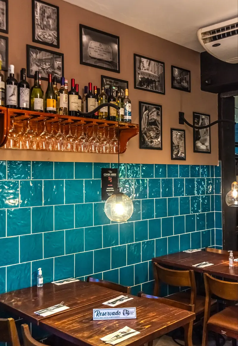 Oggi Leblon, com azulejos verde-água, vinhos na parede e quadros em preto e branco